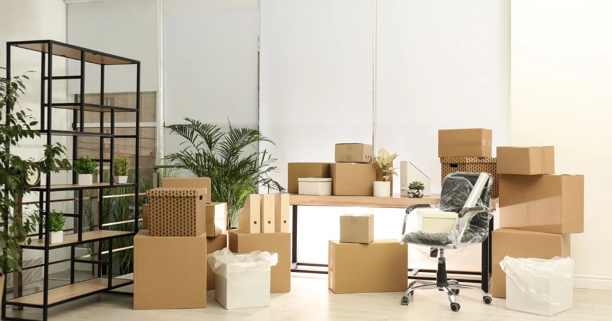 Office being packed for relocation with boxes, a wrapped desk chair and shelving