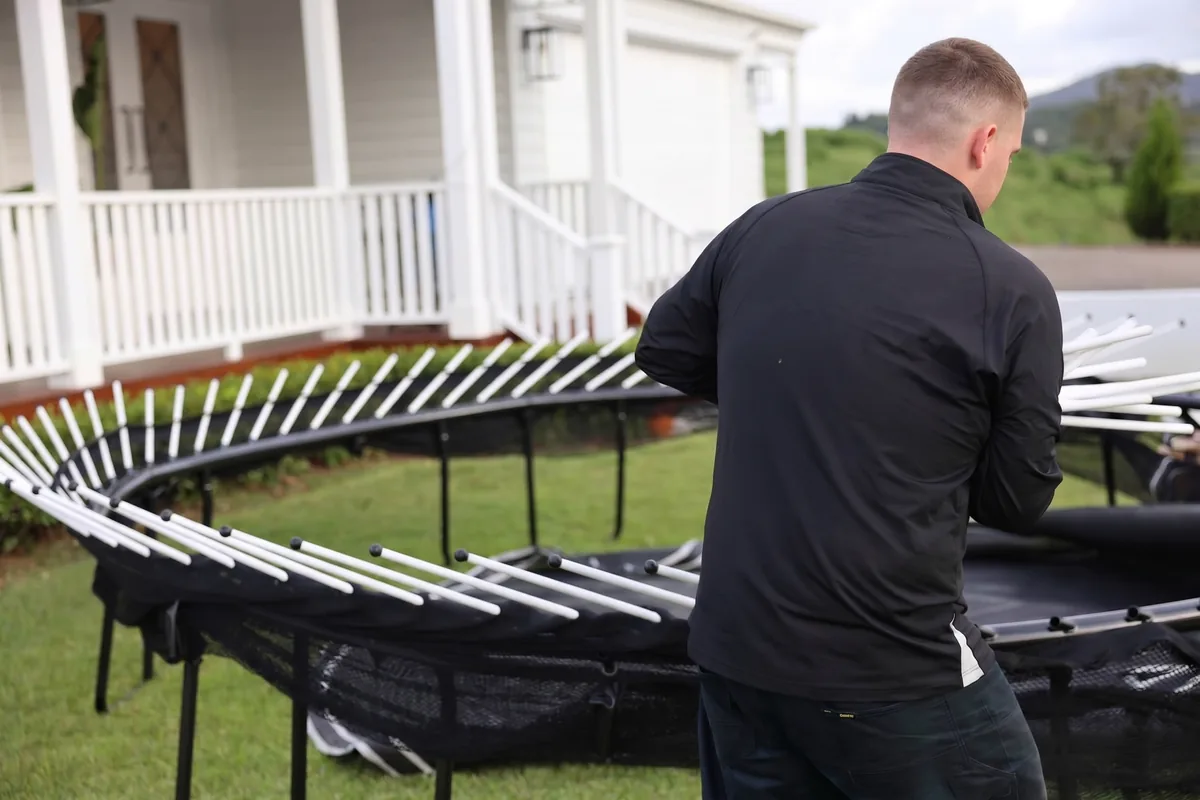Next Phase Moving technician laying out the frame and enclosure poles of a trampoline in a customer's back yard